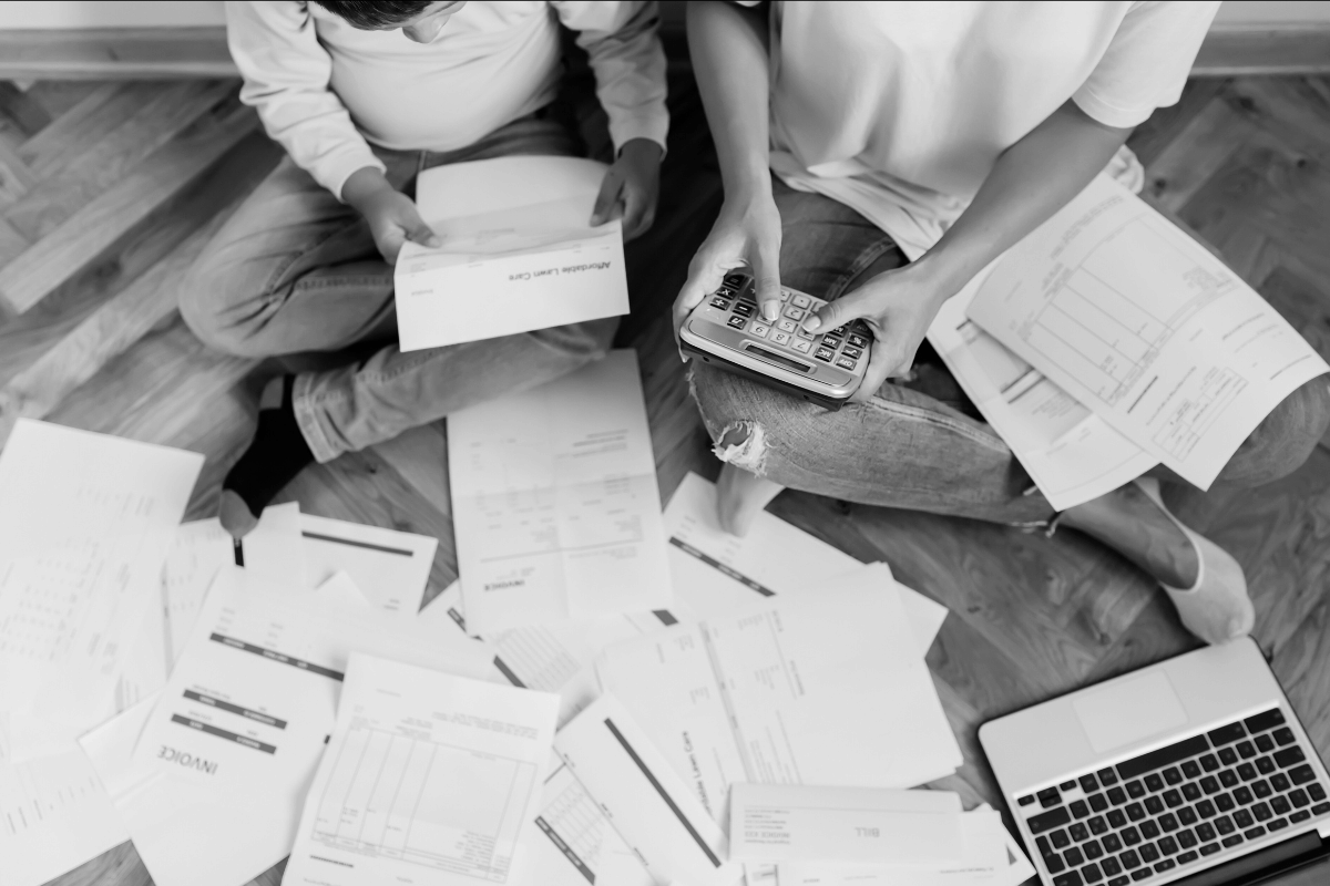 Black and white photo of a couple sitting on the floor surrounded by bills, paying off all their debt