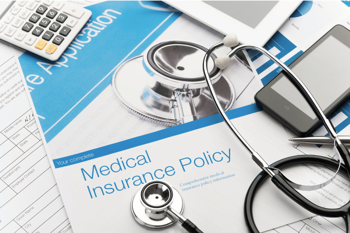 Insurance policy paperwork on a doctor's desk amid stethoscope, phone, and calculator