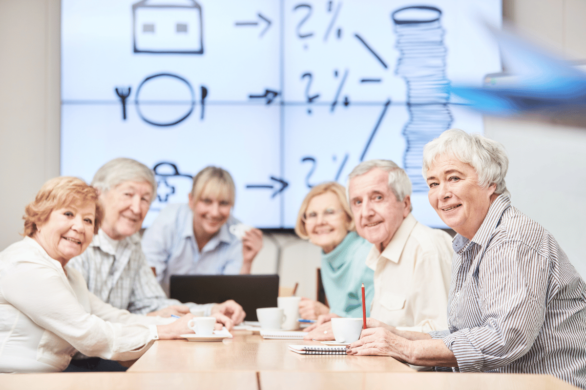 Group of seniors sharing life and financial advice at a table in front of a screen