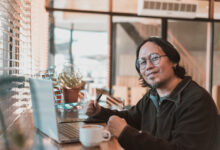 A middle aged asian graphic designer freelancer with a laptop and drawing tablet. Working remotely at a coffee shop or cafe.